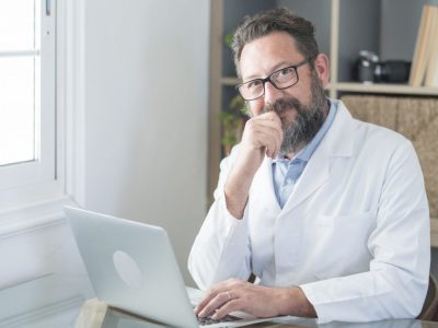 smiling-old-male-doctor-in-glasses-and-white-uniform-sit-at-desk-in-hospital-work-on-laptop.jpg smiling-old-male-doctor-in-glasses-and-white-uniform-sit-at-desk-in-hospital-work-on-laptop.jpg